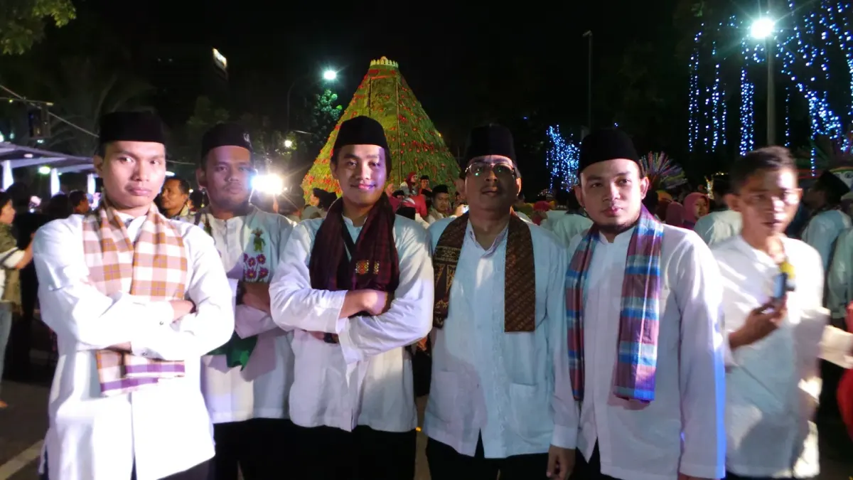 Sekelompok pemuda berbaju koko putih lengan panjang dengan kain kotak-kotak tersampir di leher dan peci hitam berpose di sebuah acara malam berlampu hias.