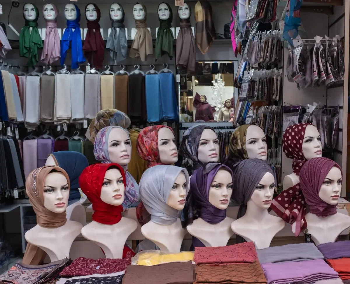 Etalase toko kain di Turki: deretan manekin kepala berjilbab beragam warna (hijau, maroon, biru, abu-abu, ungu, merah) dan tumpukan kerudung terlipat.