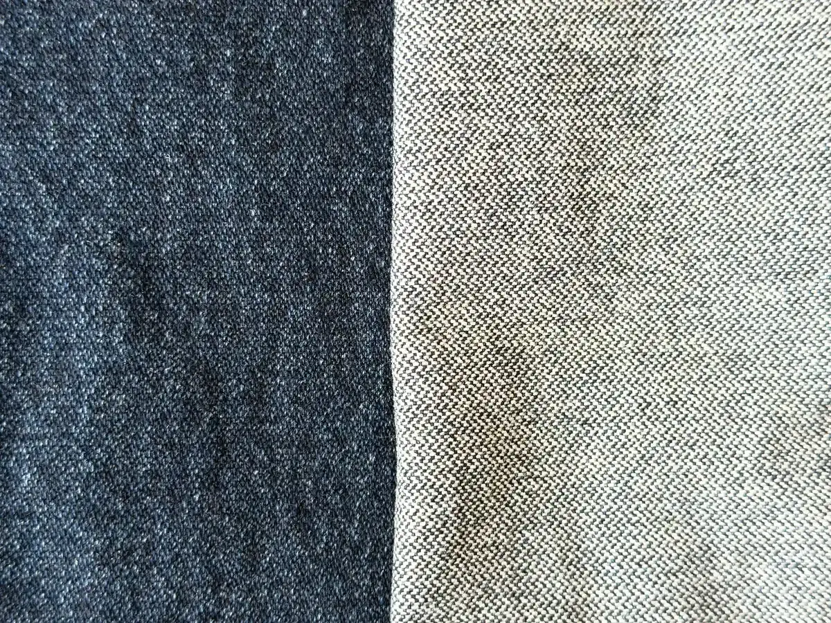 Dua sisi kain denim berdampingan, sisi luar biru indigo tua di kiri dan sisi dalam yang jauh lebih terang keputihan di kanan, dengan tekstur anyaman diagonal.