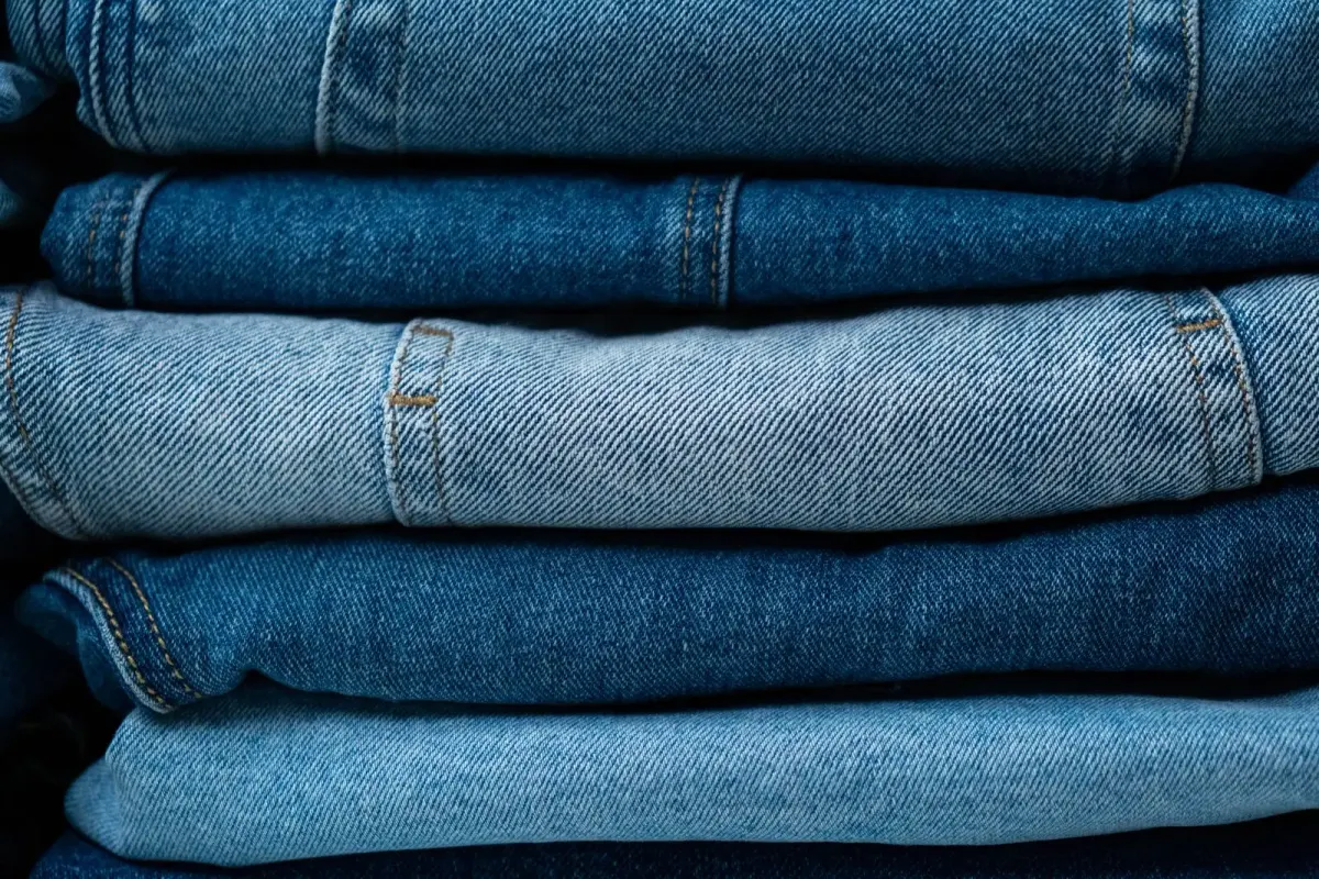 Tumpukan beberapa celana jeans biru yang dilipat, dari warna biru muda pudar sampai biru tua, terlihat dari samping.