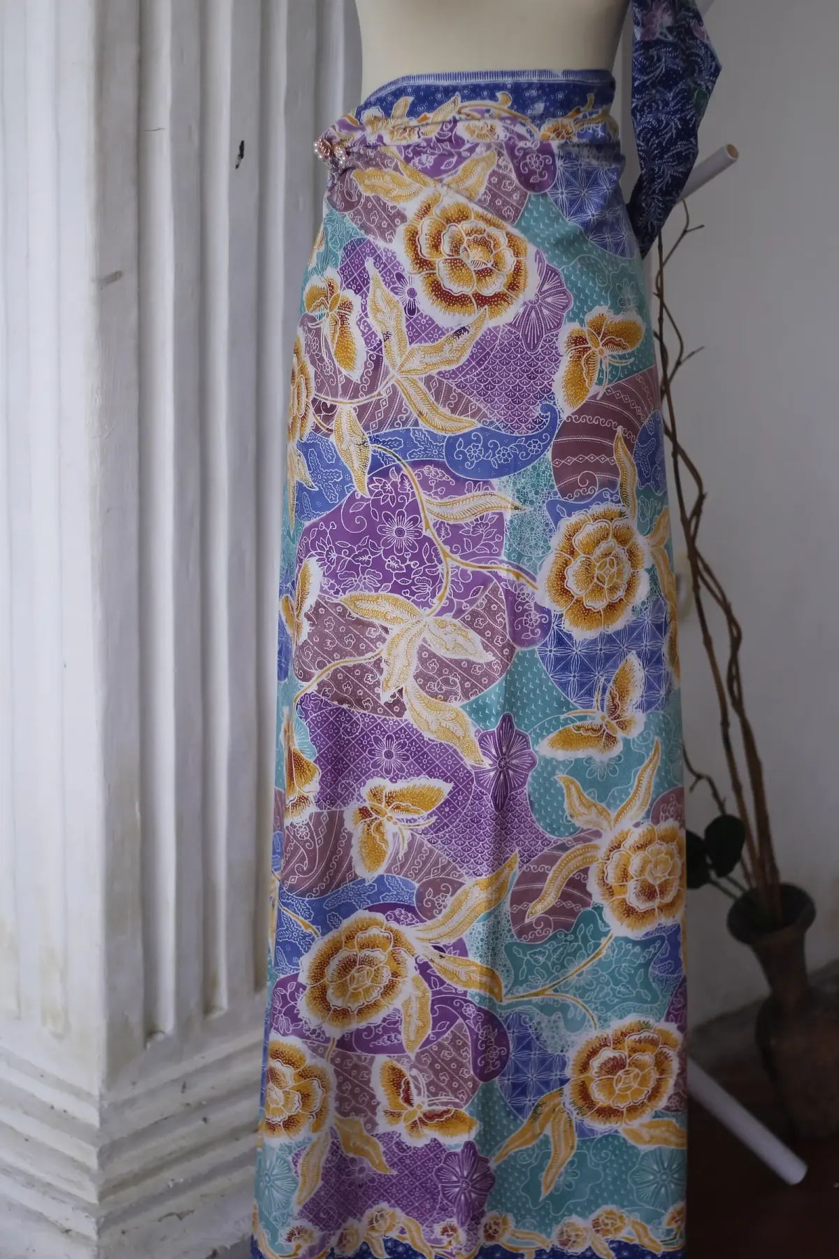 Kain jarik batik Lasem bermotif bunga besar kuning keemasan di atas latar ungu, biru, dan tosca, dililitkan pada manekin sebagai bawahan panjang.