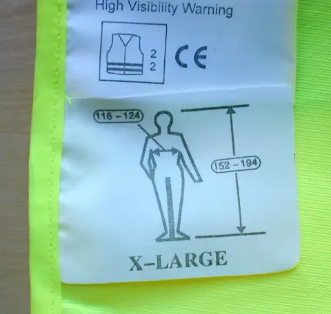 Label ukuran X-LARGE pada pakaian kuning visibilitas tinggi dengan piktogram tubuh, angka 116-124 di garis dada dan 152-194 untuk tinggi badan.